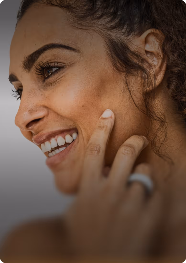 Close-up of a smiling woman touching her cheek with her hand wearing a gray ring.